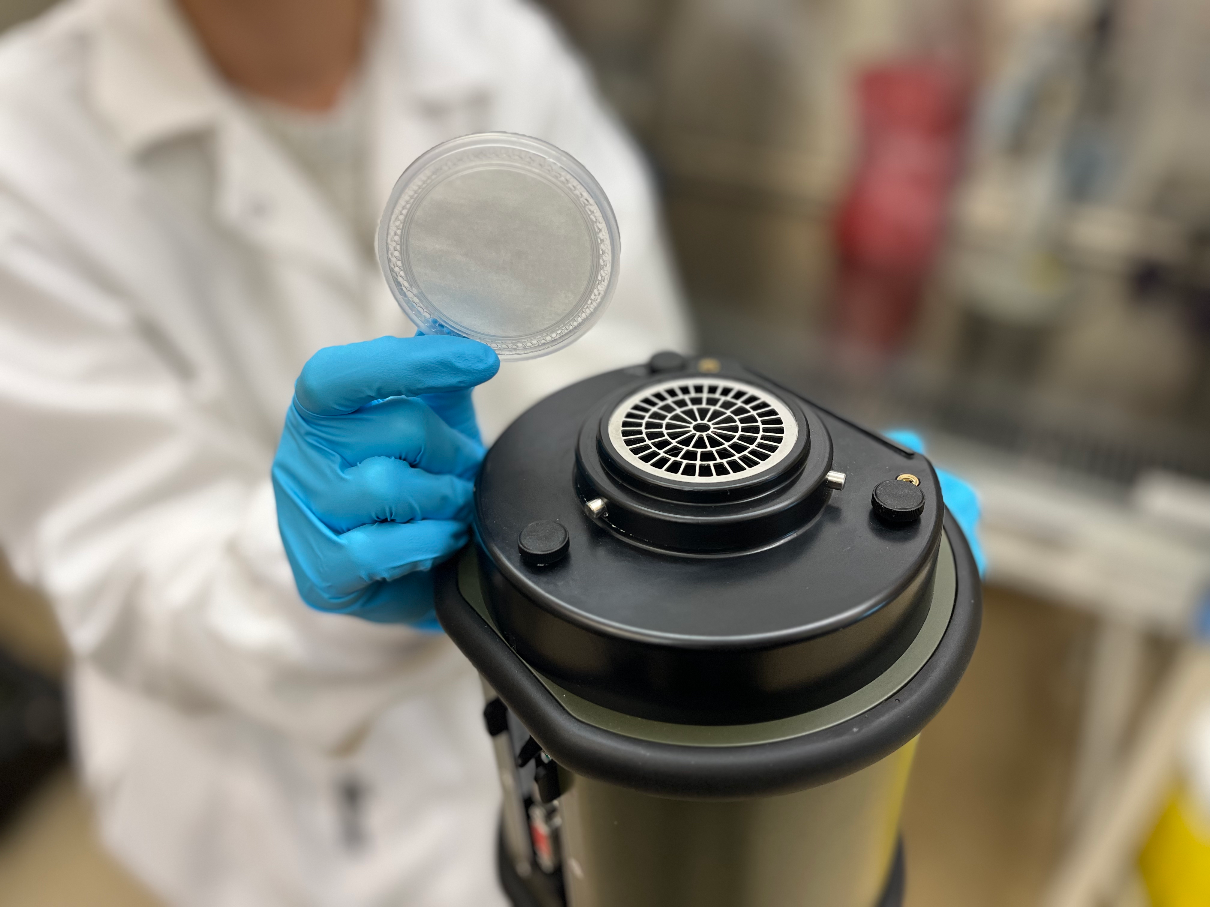 Gloved hand holding filter above air sampler